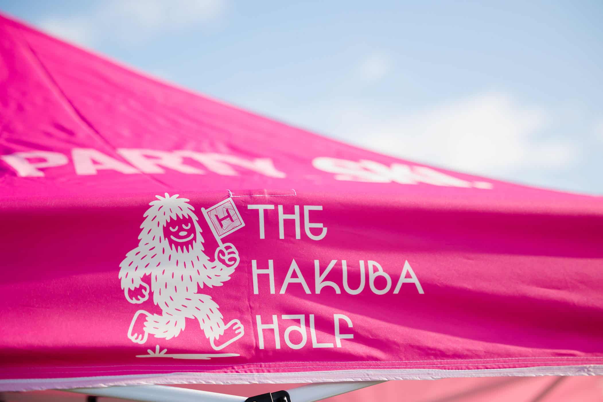 The Hakuba Half Marathon event logo featuring a white running yeti mascot holding a flag on a hot pink background.